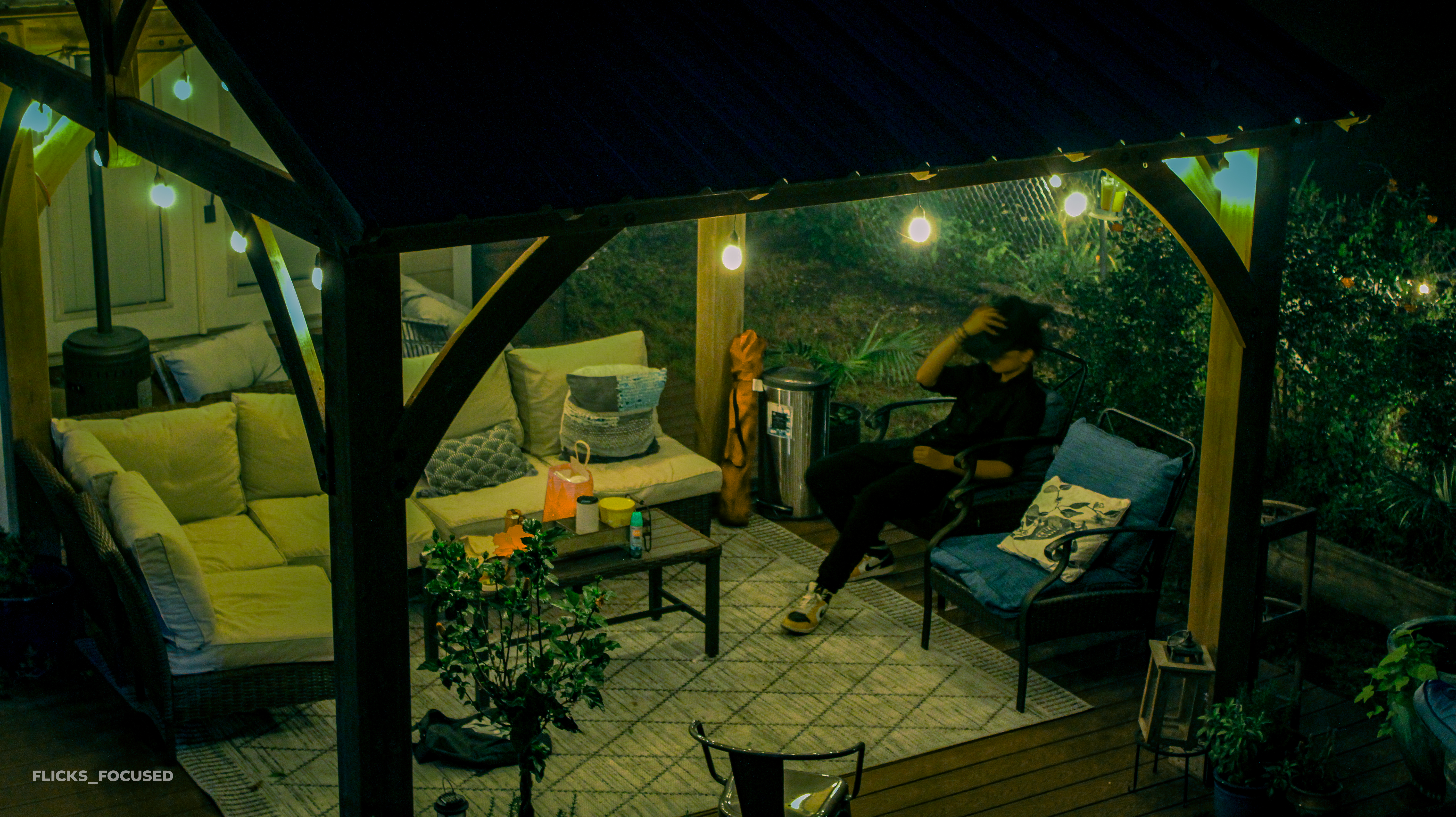 Person relaxing under a gazebo with string lights